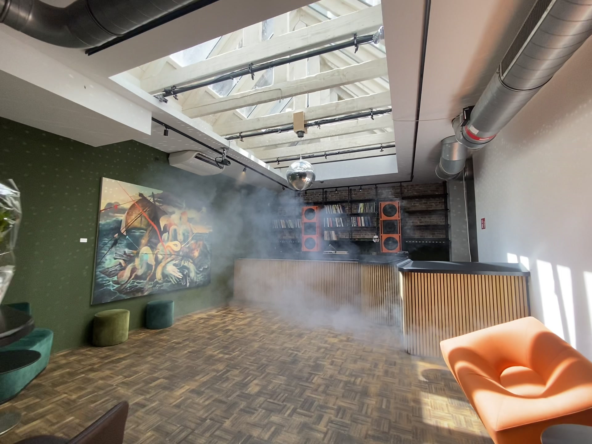 The SHELTER main room by day: sunlight through the skylight, haze drifting past the mural and the disco ball, the orange speakers at the back